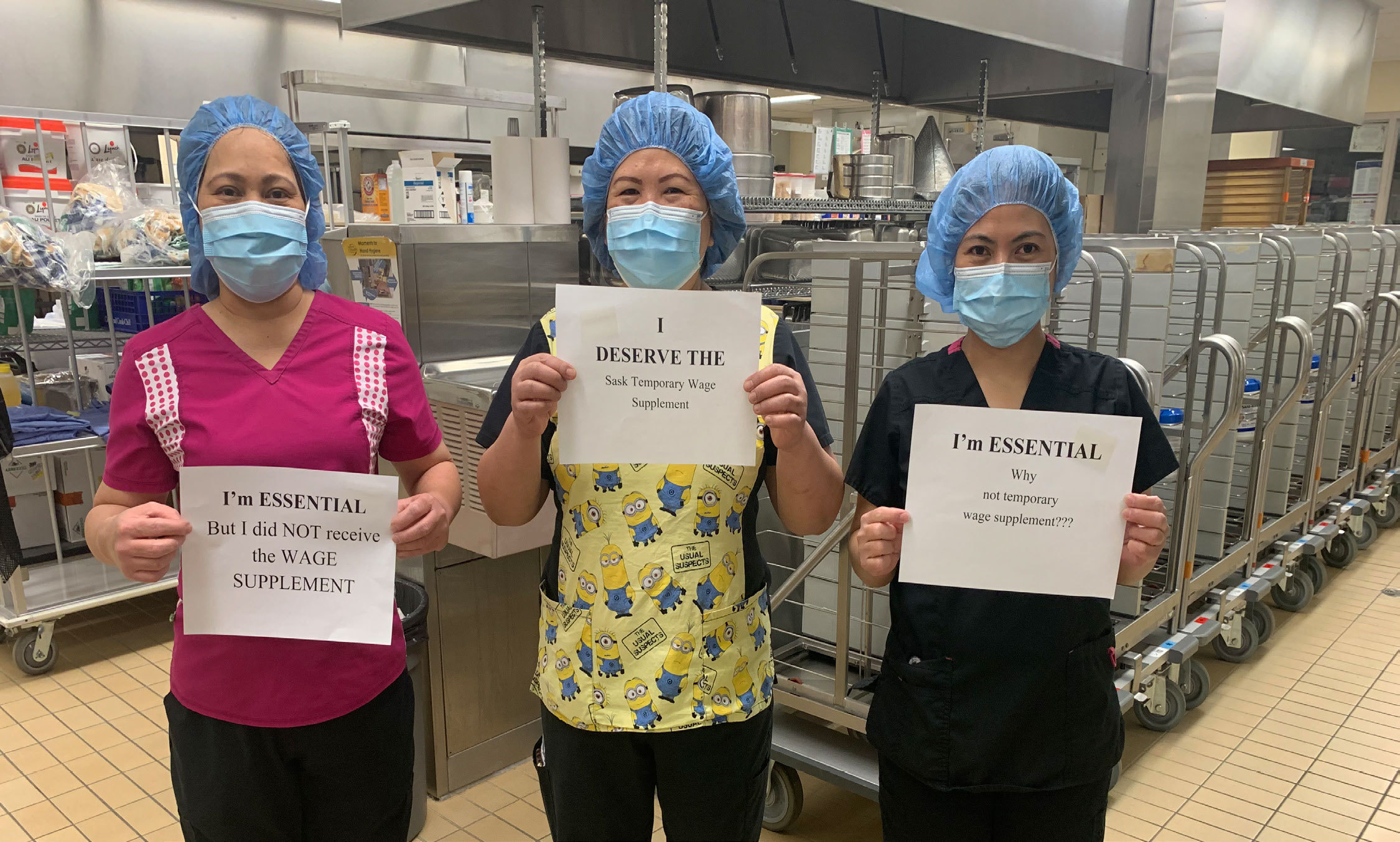 Three women in PPE holding signs which read I'm Essential.